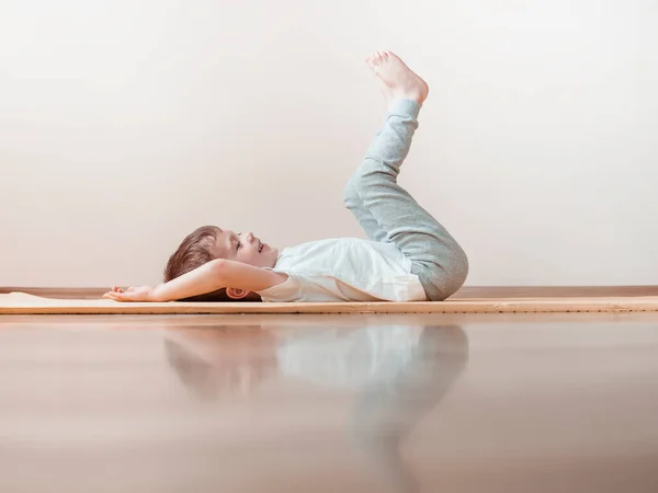 Young boy laying on a Happy Baby Pose and doing yoga exercises at home — Stock Photo, Image