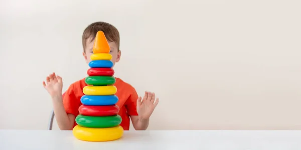 Games for the self-development of children, banner with copy space. Happy boy collects a colorful pyramid