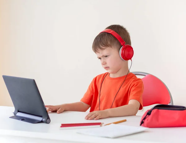 Verward 5-jarige jongen luistert naar een leraar over online communicatie via een tablet pc. Draagt een koptelefoon. Online leren. E-studie thuis — Stockfoto