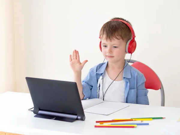 E-studeren thuis. 5-jarige jongen maakt gebruik van een tablet thuis, steekt zijn hand op voor het antwoord op een virtuele online klasse — Stockfoto