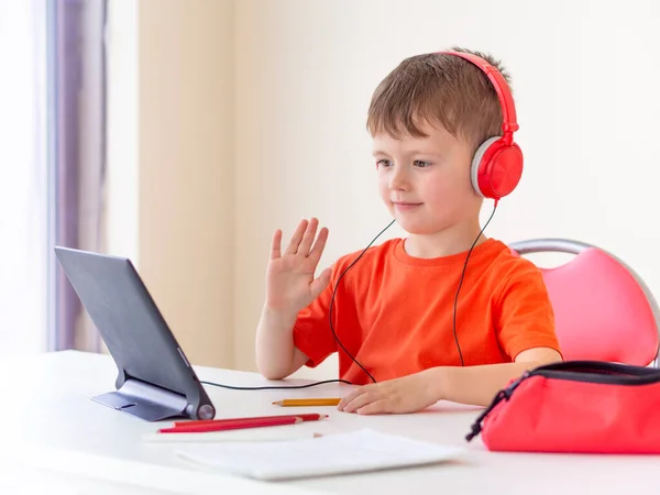 Online studeren voor kinderen. Jonge jongen gebruikt een tablet thuis, steekt zijn hand op online klasse. Onderzoek thuis tijdens quarantaine- en coronavirusepidemie — Stockfoto