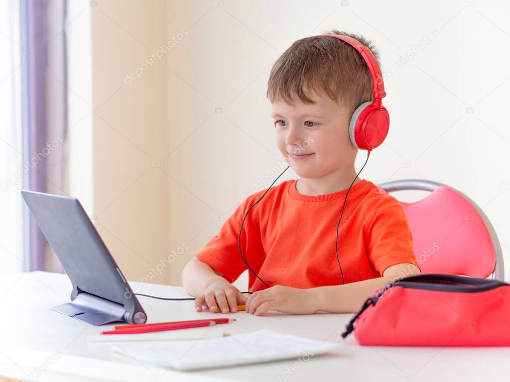 E-learning for kids. Young boy wearing headphones uses a tablet at home. Study Online during Quarantine and coronavirus epidemic
