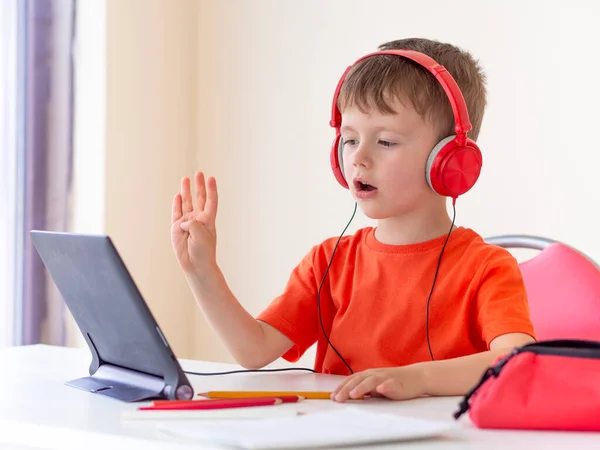 Online cursussen voor kleuters. 5 jaar jongen gebruikt een tablet thuis, steekt zijn hand op en beantwoordt de vraag van de leerkrachten — Stockfoto