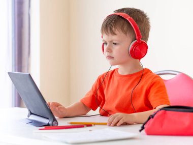 Anaokulu e-öğrenme konsepti. Çocuk kulaklık takıyor ve tablete bakıyor.