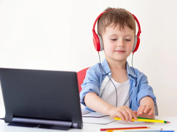 Anaokulu çevrimiçi öğrenme konsepti. Çocuk kulaklık takıyor ve bir kalem alıyor. Tabletteki bir öğretmenle yayın izliyoruz. — Stok fotoğraf