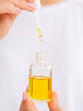 Sarı kozmetik yağıyla açılan şişeyi kapat. Kadın elinde bir damlalık tutuyor. Logonuz için yer