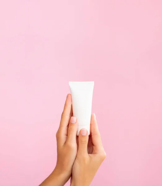 Vertical cosmetic banner mockup. Beautiful female hands show a white clean tube of cream. Copy space for promo text and your logo