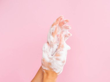 El yıkama konsepti. Pembe arka planda sabun köpüğü olan kadın eller.