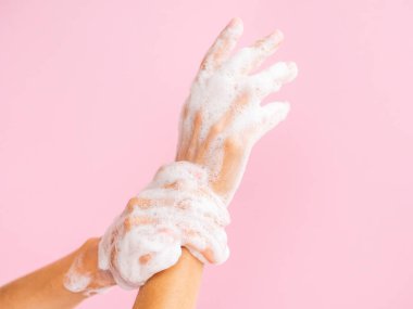 Coronovirüs konsepti sırasında el dezenfeksiyonu. Pembe arka planda sabun köpüğü olan kadın elleri.