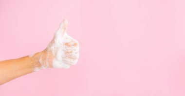 El yıkama konsepti. Kadınsı sabunlu el, başparmağı havada ve pembe arka planda bir afiş için fotokopi alanı. Tanıtım için alanı kopyala