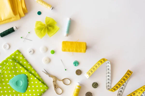 Frame met set groene en gele accessoires voor het naaien op een witte ondergrond. Bovenaanzicht, vlak lay — Stockfoto