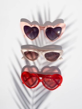 Yaz moda konsepti. Beyaz arka planda palmiye yaprağı gölgesi olan şık kadın güneş gözlükleri.