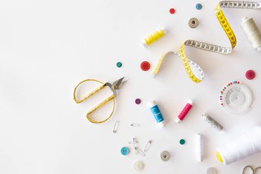 Evde dikiş dikiyorum. Beyaz masa üzerinde dikiş araçları ve aksesuarların üst görünümü