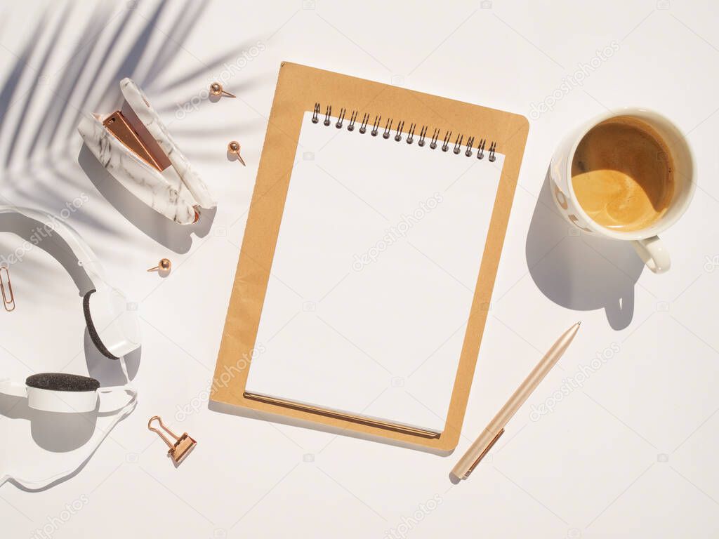 Woman stuff background and feminine desk. Opened notebook with copy space, cup of coffee, earphones and trendy palm branch shadow. Flat lay on a white background