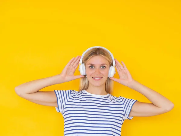 Concept de style de vie musical. Fille souriante regardant la caméra tout en touchant casque sans fil blanc sur fond jaune — Photo