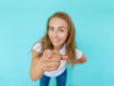 Jest konseptine puan. Gülümseyen kız seni işaret ediyor, seni istiyor, renkli stüdyo arka planında bulanık bir portre. Bokeh etkisi, parmağa odaklan