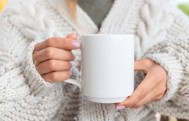 Beyaz seramik kupa modeli. Süveter giyen kadın elinde bir fincan sıcak kahve tutuyor. Yazdırmak için boşluk kopyala