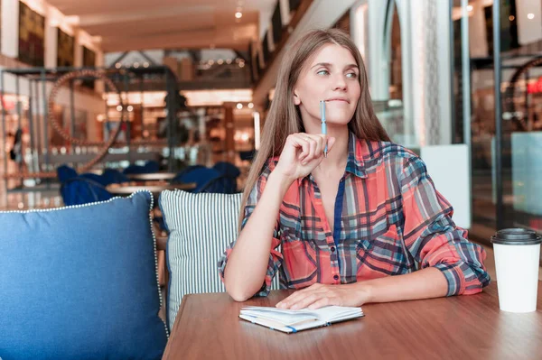 Dreams and pensive facial expression. Young woman with pen and notebook sitting on cafe and dreaming