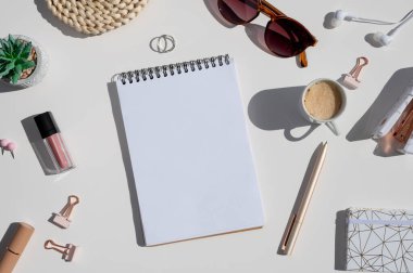 Kadınsı yaratıcı çalışma alanı modeli. Kadın aksesuarlarıyla güneş ışığında beyaz masa spiral defter ve bir fincan kahve açtı.
