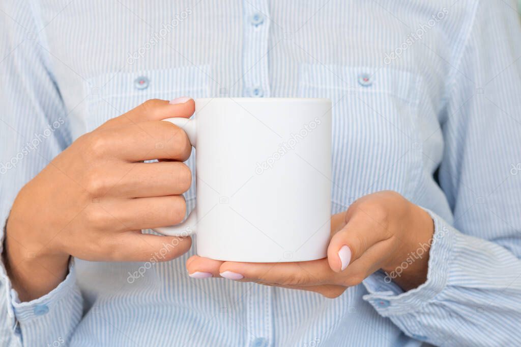 White ceramic mug mockup. Girl wears blue shirt Holds a Cup of cocoa. Space for your text branding