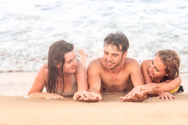 Concepto de vacaciones de verano. Jóvenes amigos - El hombre y las niñas se divierten en la playa, acostado en la arena de oro — Foto de Stock