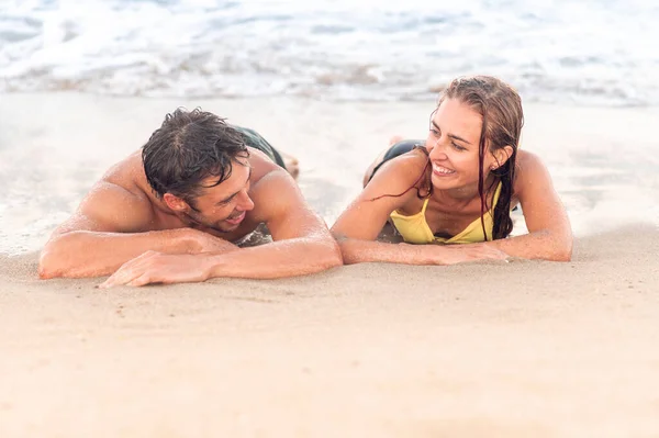 Concepto de vacaciones de verano. Retrato de una joven pareja feliz en la playa, tendida en la arena cerca del agua — Foto de Stock