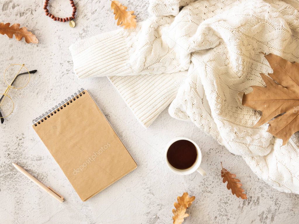 Autumn is coming. Cozy composition with notepad, cup of coffee over knitted sweater with autumn leaves