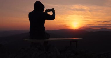 Yanan günbatımının, gökyüzünün ve dağ tepelerinin panoramik manzarasının fotoğraflarını yapan adam.