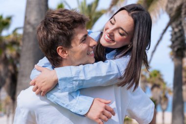 Palmiye ağaçlı mutlu genç çift, arkadan sarılan kadın, yaşam tarzı, romantizm, eğlence, modern aşk, yaz eğlencesi, güven, şefkat, pozitif duygular, modaya uygun insanlar