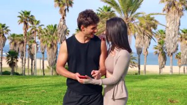 Atletik çift birbirine sarılıyor ve neşeli bir selfie çekiyor. Deniz kenarındaki yemyeşil bir palmiye bahçesinde kırmızı bir akıllı telefon ile yaz aşkını, sporu, seyahat anılarını ve canlı açık hava yaşam tarzını kutluyorlar..