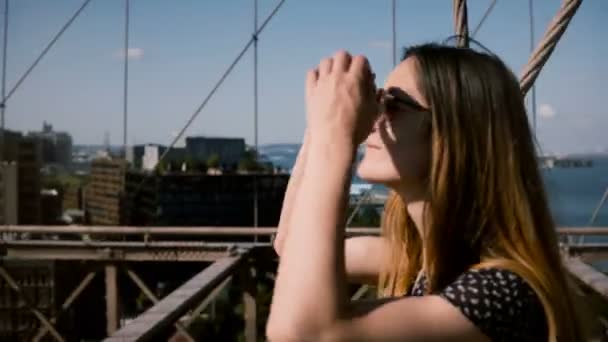 Brooklyn Köprüsü 4 k yürüyüş altın saçlı güzel mutlu Avrupa kız vintage güneş gözlüğü kamera izler. — Stok video