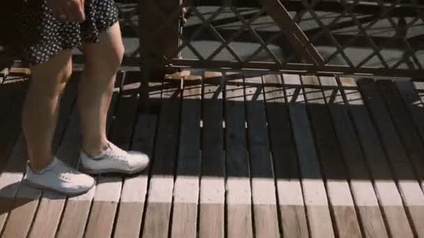 Cámara inclina hacia arriba siguiendo a joven mujer turista feliz en gafas de sol caminando a lo largo del puente de Brooklyn disfrutando de la vista 4K . — Vídeo de stock