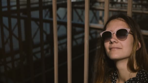 Jovem turista europeia positiva em óculos de sol elegantes sorrindo, olhando para cima apreciando a vista no Brooklyn Bridge 4K — Vídeo de Stock