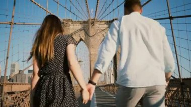 Romantik Çift Brooklyn Köprüsü Nyc yürümek, el ele tutuşup güzel bir yaz günü, arkadan görünüm düşük açılı 4 k öp.