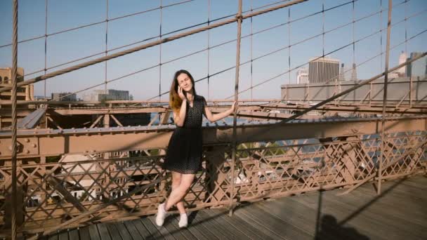 Atractiva joven europea hablando por teléfono, de pie en la increíble vista del puente de Brooklyn en un hermoso día de verano 4K — Vídeo de stock