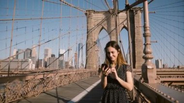 Brooklyn Köprüsü, New York City'de 4 k smartphone görüntülü arama app kullanarak arkadaşlarınıza çekici yetişkin Avrupa kadın konuşuyor.