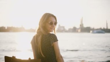 Güzel Avrupa kadın güneş gözlüğü geri kameraya bakar, güneşli şehir sahilde arkasını dönüyor. Yaz gün batımı 4 k zevk.