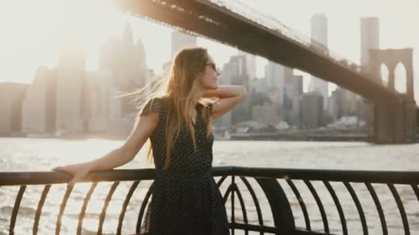 Mulher branca bonita com o cabelo soprando no vento posando para a câmera no incrível cais do rio por do sol New York 4K — Vídeo de Stock