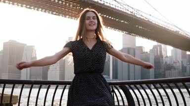 Güzel mutlu beyaz kız doğal günbatımı nehir setin Brooklyn Köprüsü, New York ağır çekim yakınındaki iplik.