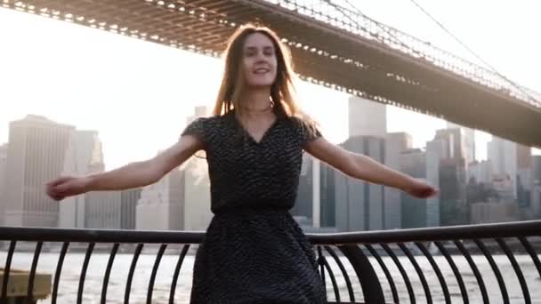 Hermosa chica caucásica feliz girando en el hermoso terraplén del río atardecer cerca del puente de Brooklyn, Nueva York cámara lenta . — Vídeo de stock