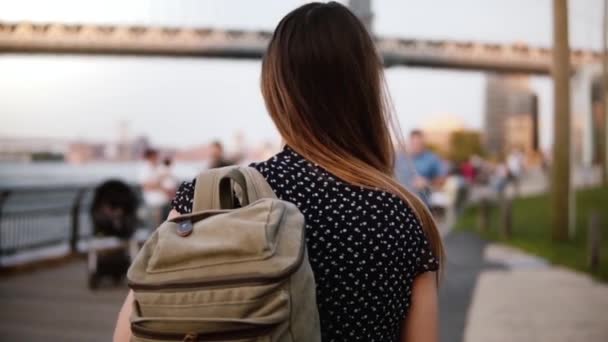 Kameran följer ung kvinnlig turist med ryggsäck i solglasögon promenader längs soliga Brooklyn Park New York slowmotion — Stockvideo