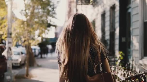 Обратно вид счастливая кавказская девушка с летящими волосами прогуливаясь по солнечной улице города, живя случайный образ жизни замедленной съемки . — стоковое видео