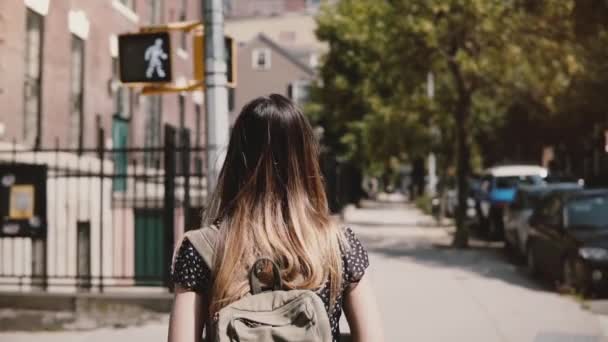 Camera follows girl with backpack walking along sunny New York street, living a casual happy lifestyle slow motion. — Stock Video