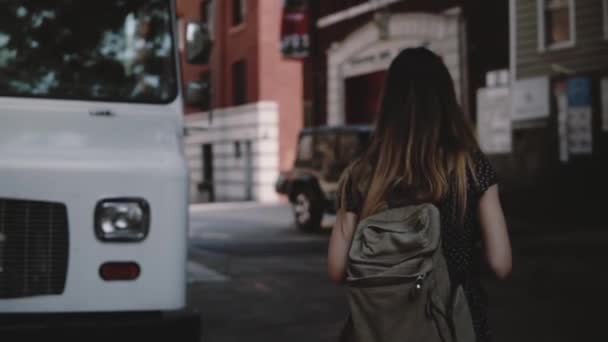 Camera follows young female tourist with backpack crossing the street near white van, enjoying leisure walk slow motion. — Stock Video