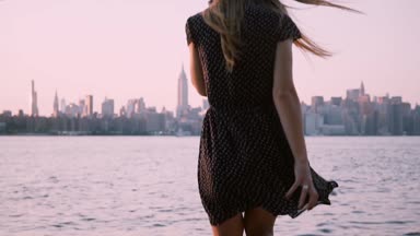 Güneş gözlüğü güzel kız aşağı su tarafından oturmak için kamera tarafından New York sahne günbatımı yavaş hareket üzerinde izlerken yürür.