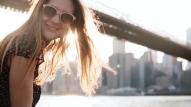 Ağır çekim mutlu girl Brooklyn Köprüsü'nün kameraya gülümseyen rüzgarda üfleme şaşırtıcı altın saçlı güneş gözlüğü.