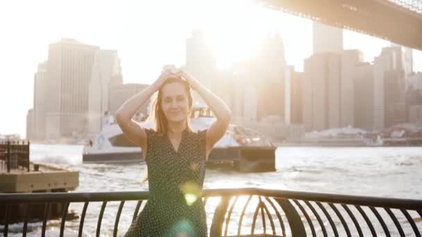 Cámara lenta hermosa mujer joven caucásica posando, tocando el pelo en increíble puesta de sol de Nueva York, grandes barcos que pasan por . — Vídeos de Stock