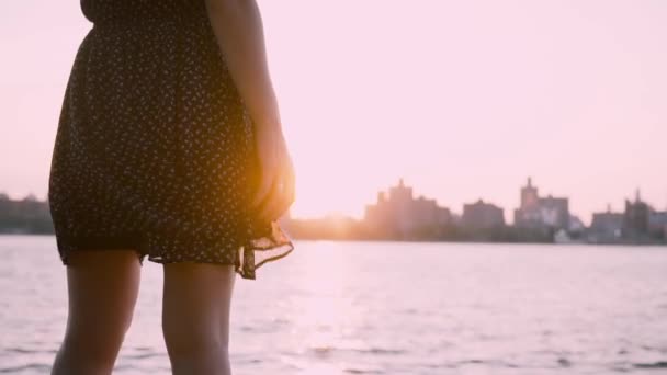 Primo piano di gambe femminili in abito nero agitando nel vento stand a bella limpida estate paesaggio urbano tramonto rallentatore . — Video Stock