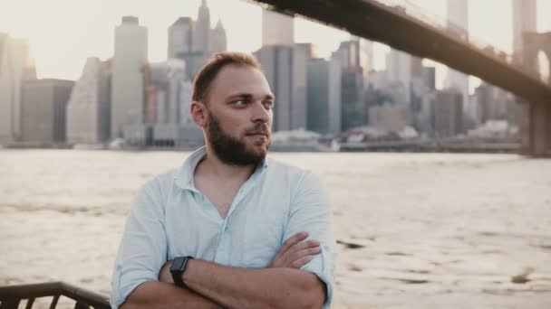 Sikeres európai freelance üzletember állandó fegyverek portréja hajtva, a Brooklyn Bridge New York folyó táj 4k. — Stock videók