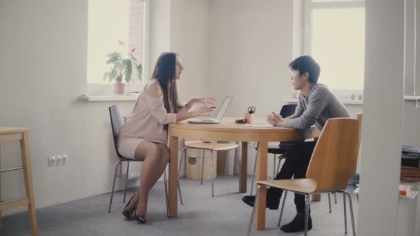 Uma advogada europeia confiante a falar com um jovem japonês à mesa. Discussão multiétnica no escritório moderno 4K . — Vídeo de Stock
